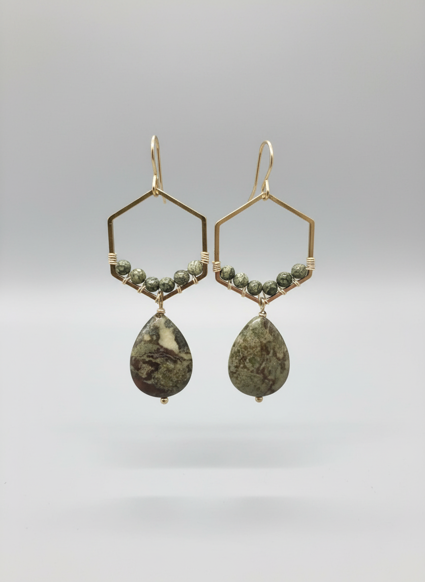 A pair of gold-colored hoop earrings with teardrop-shaped drops, potentially made of gold or gold-plated metal, against a black background.